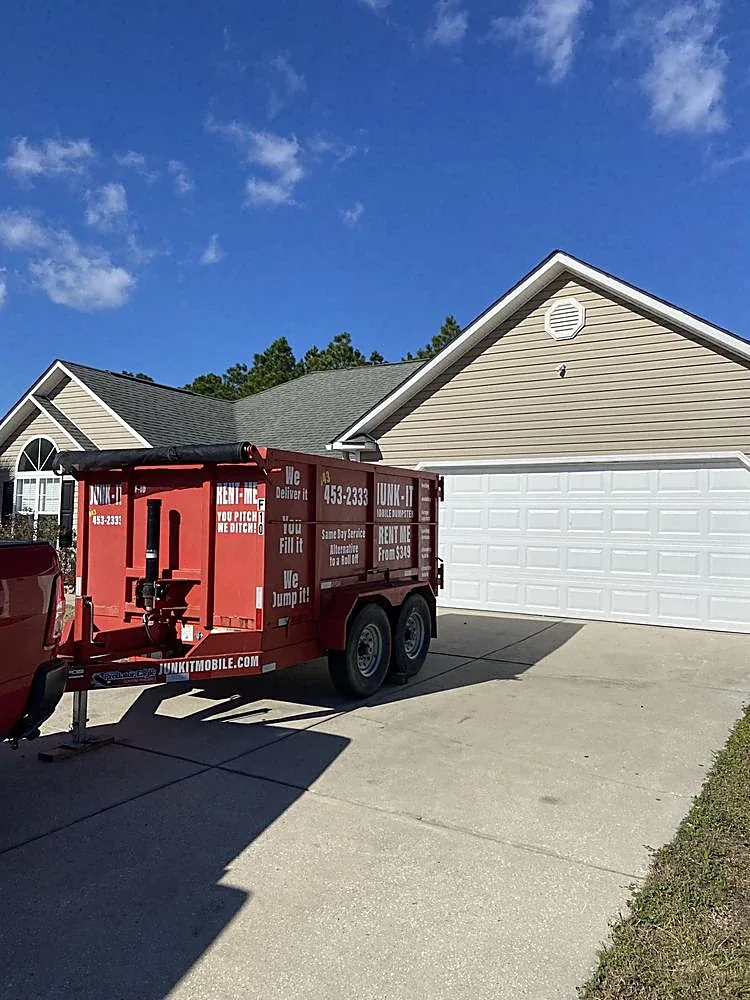 A Junk It mobile dumpster on its trailer tires, parked on the concrete driveway of a Myrtle Beach area home